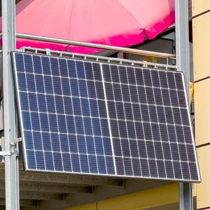 Die Solarpanels auf dem Balkon reflektieren das Sonnenlicht, während ein auffälliger pinker Sonnenschirm im Hintergrund sichtbar ist.