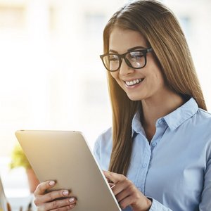 Mit einem freundlichen Lächeln interagiert die Frau mit ihrem Tablet, während sie in einem hellen, einladenden Büro sitzt.