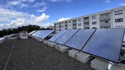 Ein Blick auf ein Dach mit Solarpanels, umgeben von einer grünen Landschaft und einem klaren blauen Himmel mit einigen Wolken.