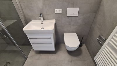 Ein minimalistisches Badezimmer-Design mit einem weißen Waschbecken, einer modernen Toilette und einer transparenten Duschkabine.